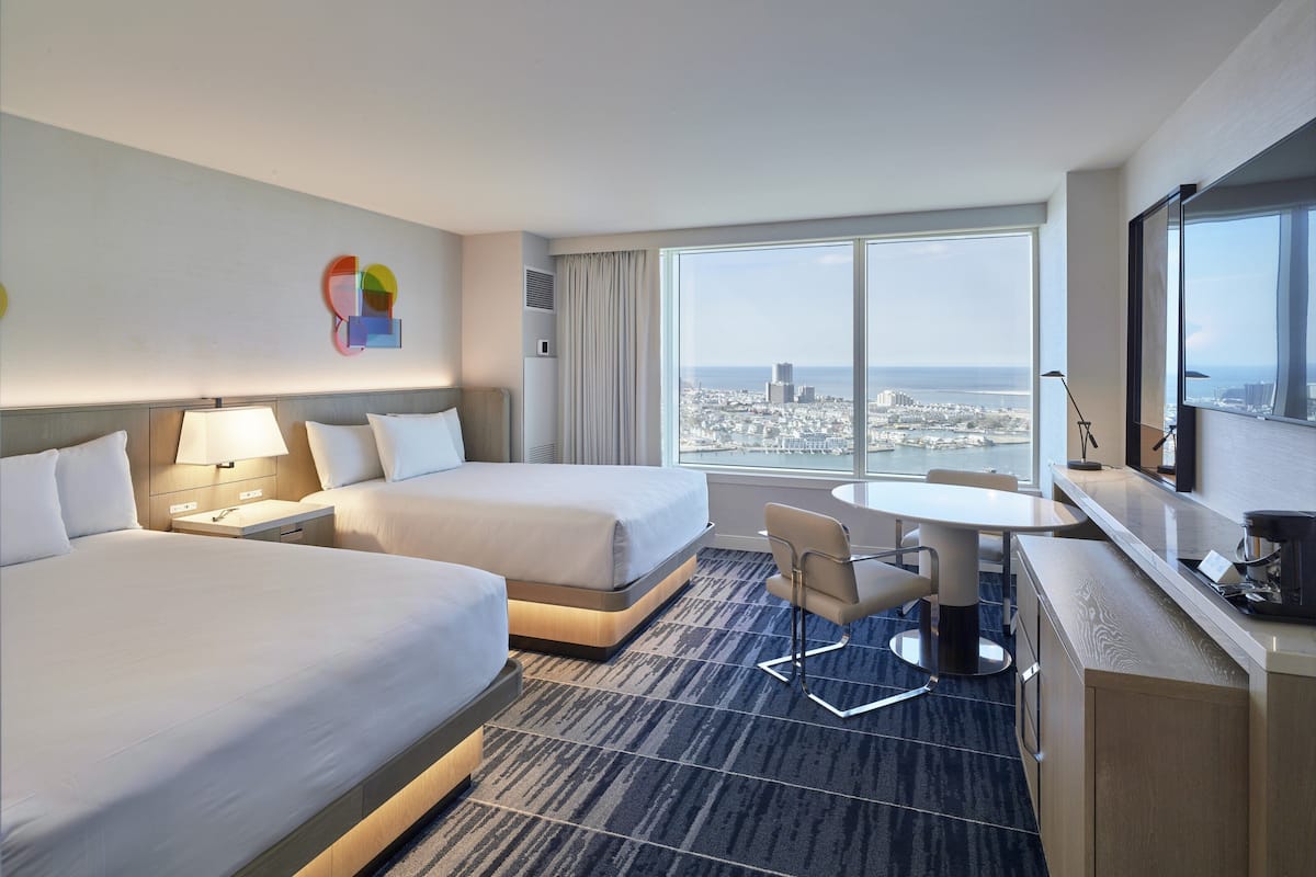 Une chambre d’hôtel avec deux lits, un bureau, une chaise et une grande fenêtre donnant sur la ville.