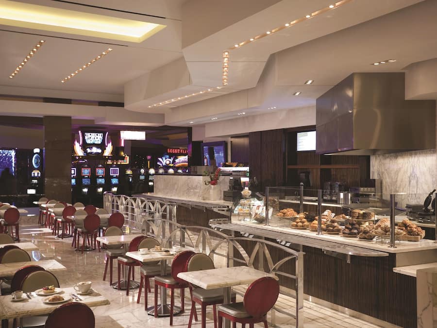 A modern restaurant with marble flooring, red chairs, and a variety of food displayed in a glass case.