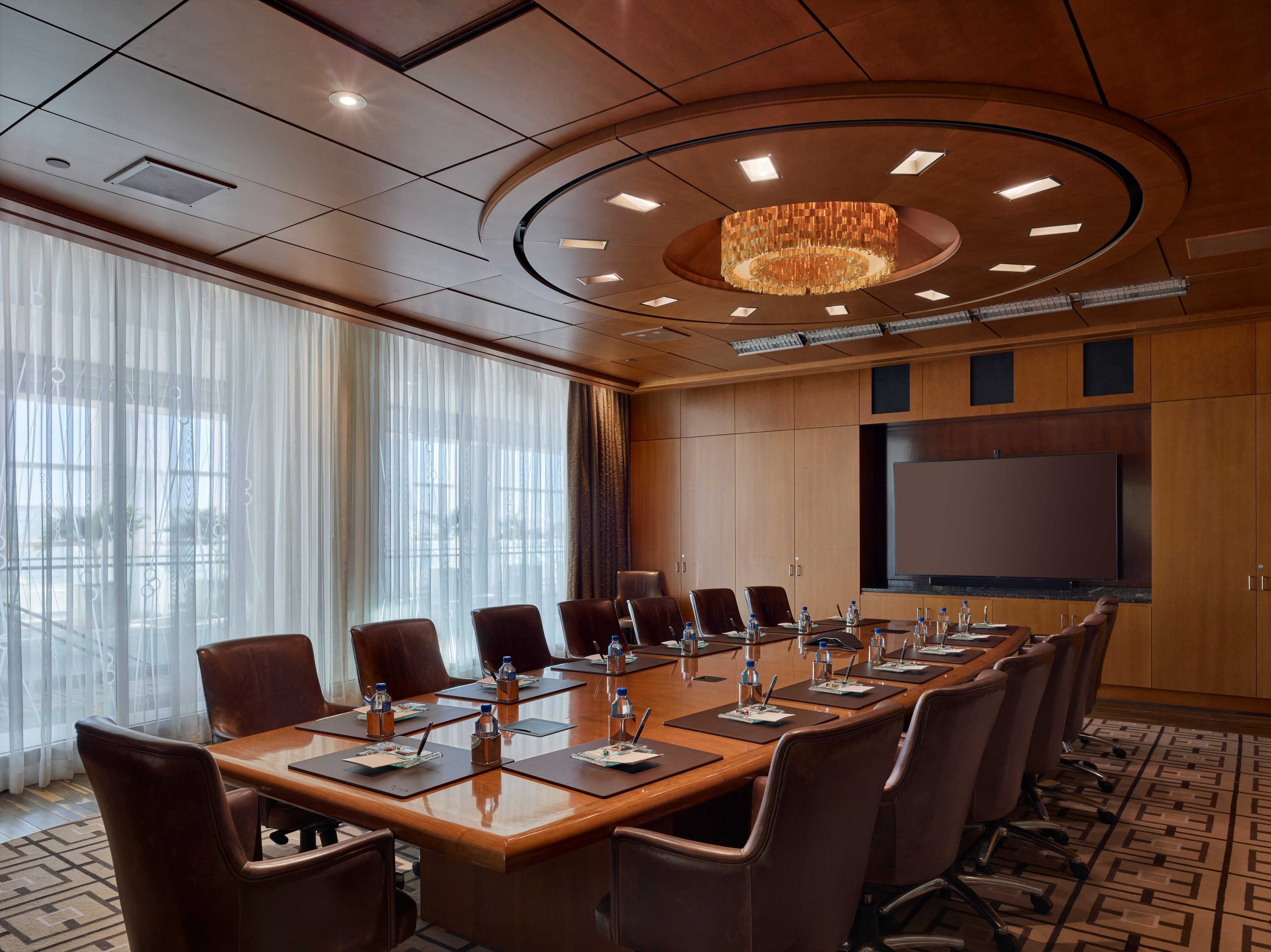 A conference room with a long table, chairs, a large screen, and a chandelier.