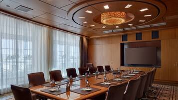 A conference room with a long table, chairs, a large screen, and a chandelier.