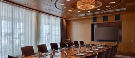 A conference room with a long table, chairs, a large screen, and a chandelier.