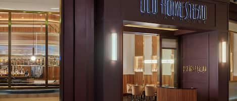 Entrada de un hotel con diseño moderno, destacando un letrero grande para 'Old Homestead Steak House'.