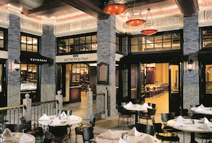Un amplio comedor interior con varias mesas y sillas, un restaurante visible llamado 'The Metropolitan' y una zona de bar con un letrero que dice 'ESPRESSO'.