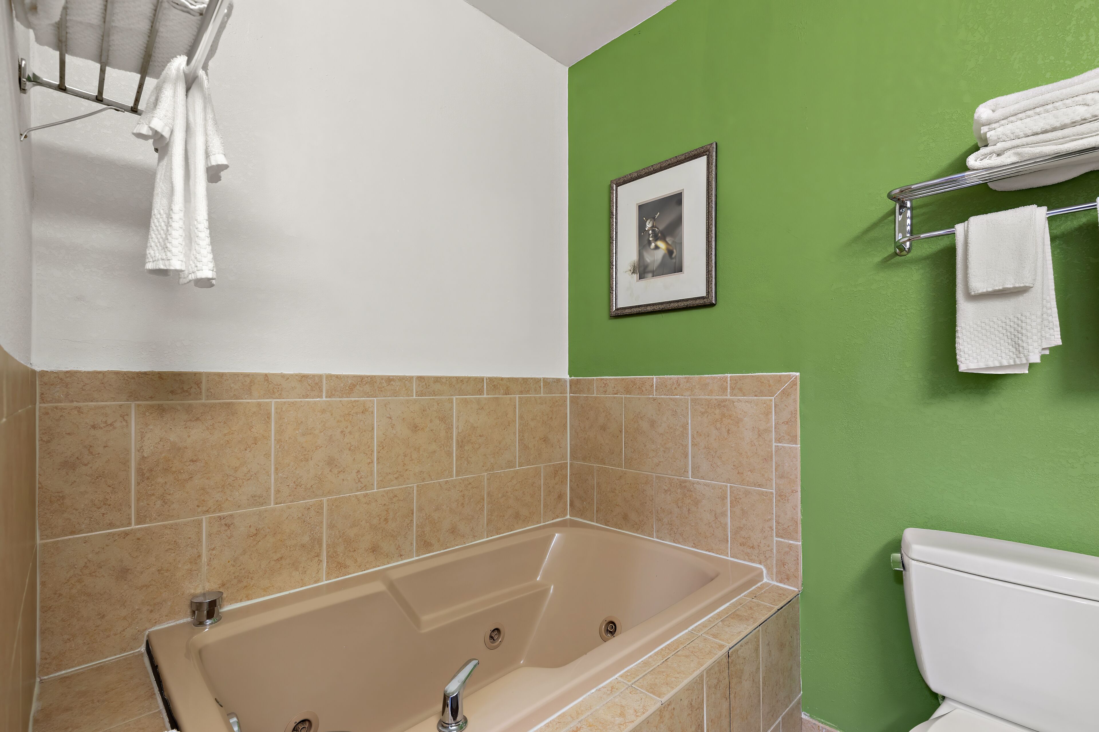 A bathroom with a beige bathtub, green walls, and a white toilet.
