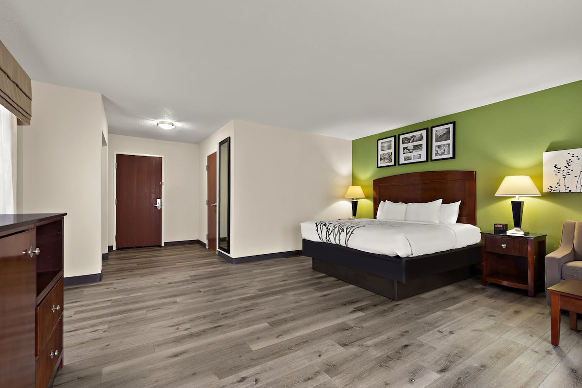 A hotel room with a bed, bedside tables, a chair, a dresser, and a door.