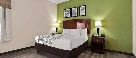 A hotel room with a large bed, two bedside tables with lamps, a green accent wall, and three framed pictures above the bed.