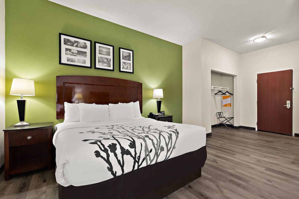 A hotel room with a large bed, two bedside tables with lamps, a wooden headboard, and green walls.