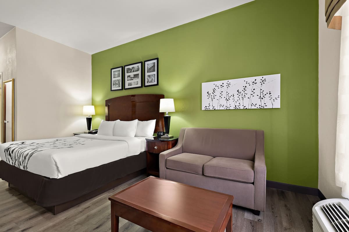A hotel room with a bed, a sofa, a coffee table, and a wall with framed pictures.