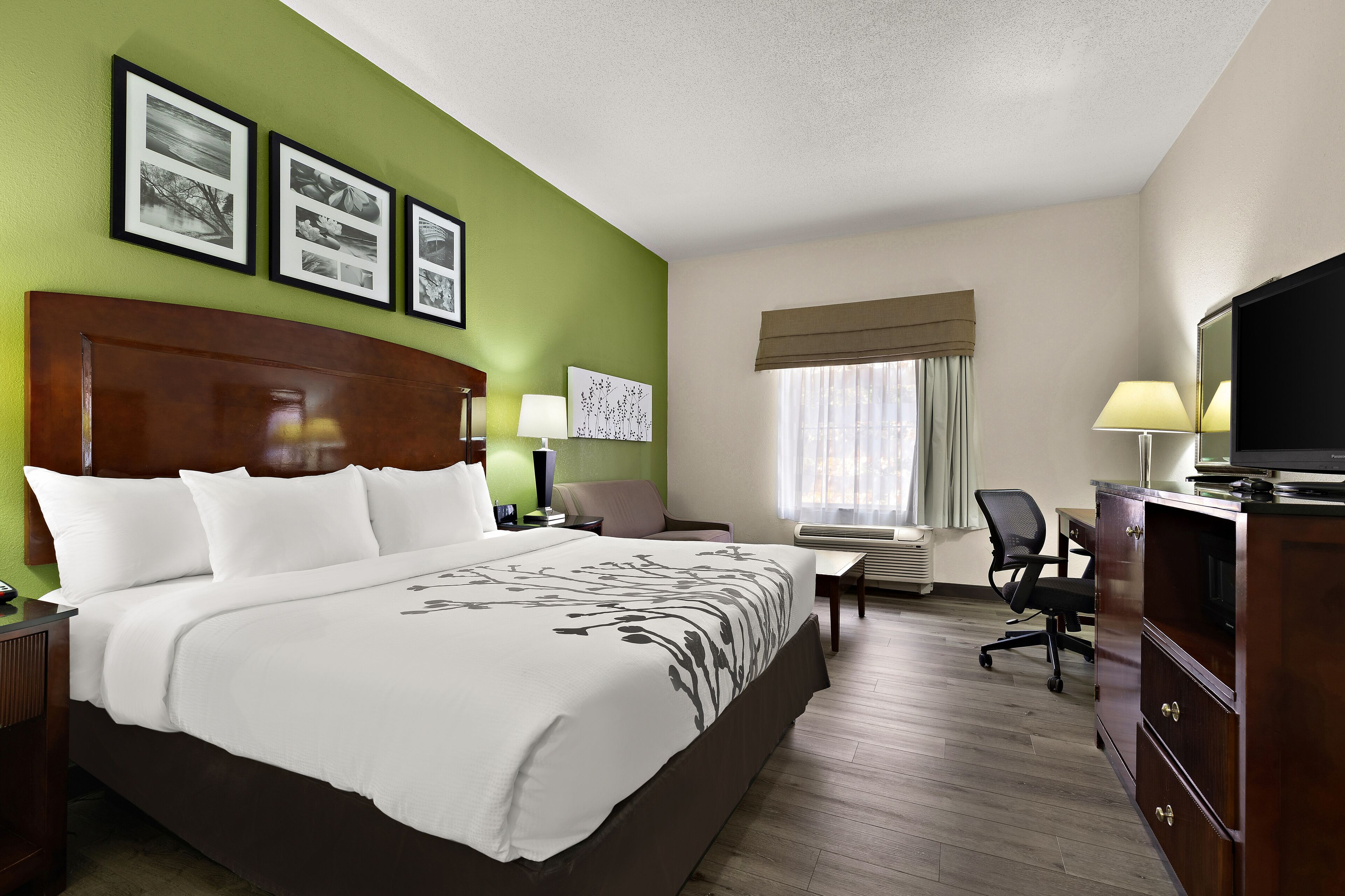 A hotel room with a large bed, a desk with a chair, a television, and framed pictures on the wall.