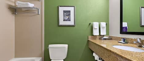 A bathroom with a green wall, a white toilet, a sink with a granite countertop, and a framed picture on the wall.