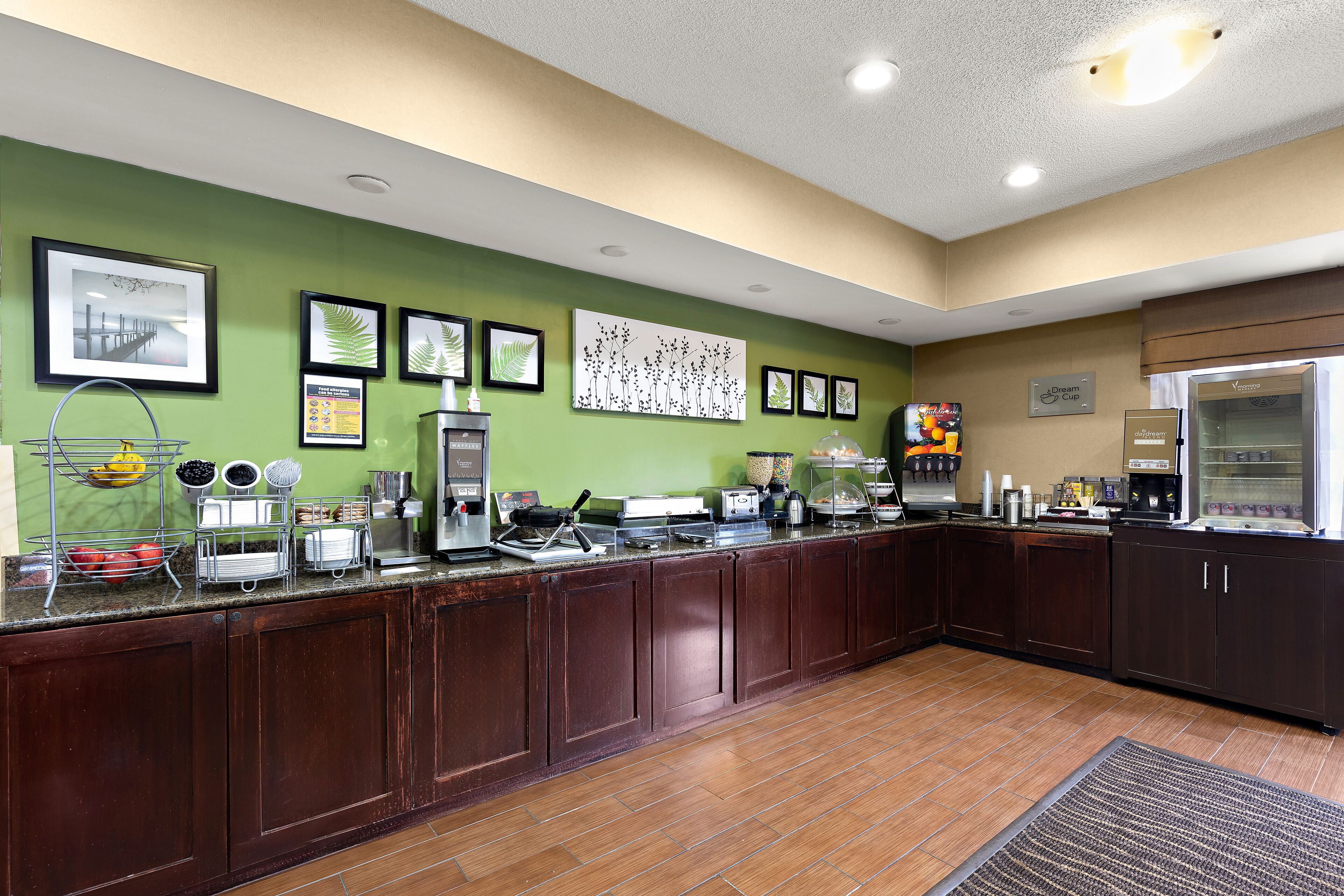 A kitchen with a green wall, framed artwork, and a coffee station.