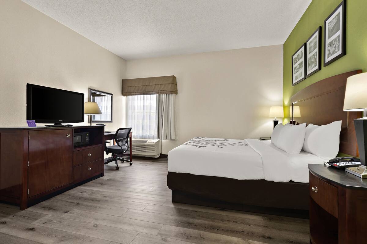 A hotel room with a bed, desk, television, and a window with curtains.