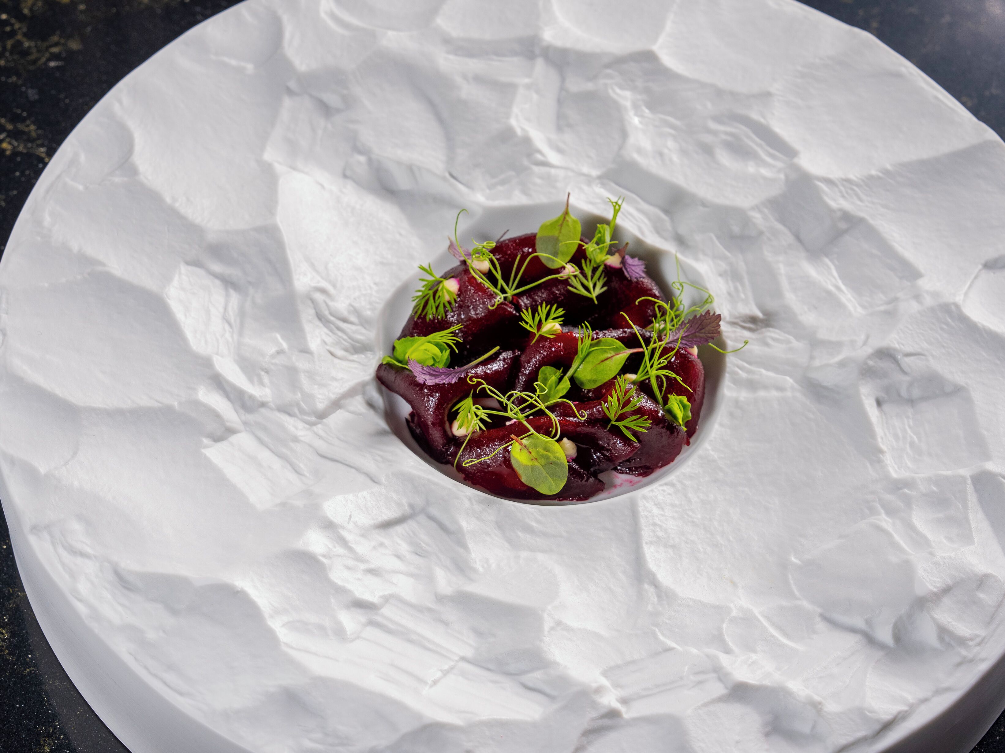 A white plate with a beet salad on a textured white surface.