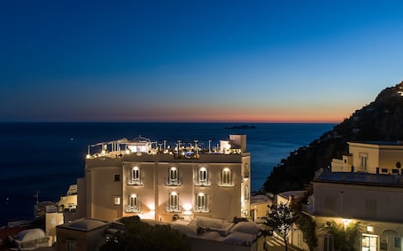 A hotel with multiple balconies overlooking the sea, featuring a rooftop bar and outdoor seating.