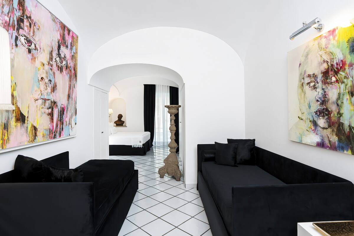 A modern living room with black sofas, a white tiled floor, and large abstract paintings on the walls.