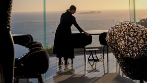 A modern interior with a glass balustrade, a person sitting by a table, and a view of the ocean. - Hotel Villa Franca (Positano)
