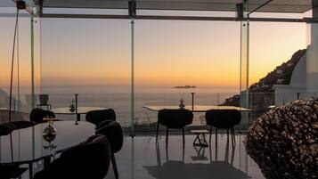 Un espace repas moderne avec une table et des chaises en verre, offrant une vue sur la côte au coucher du soleil.