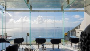 A terrace with a glass balustrade overlooking the sea, furnished with black chairs and a glass table. - Hotel Villa Franca (Positano)