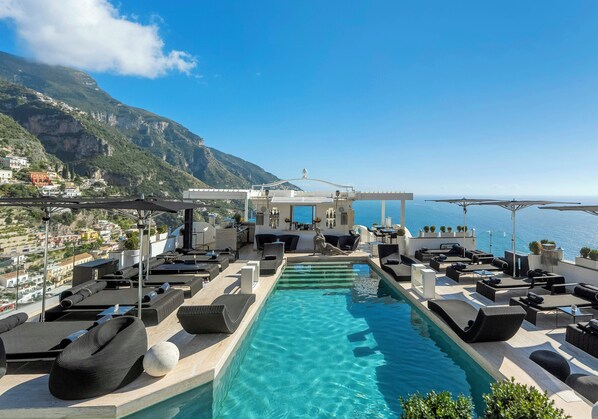 Una piscina infinita en la azotea con sillones de descanso y vistas al mar y a las montañas.