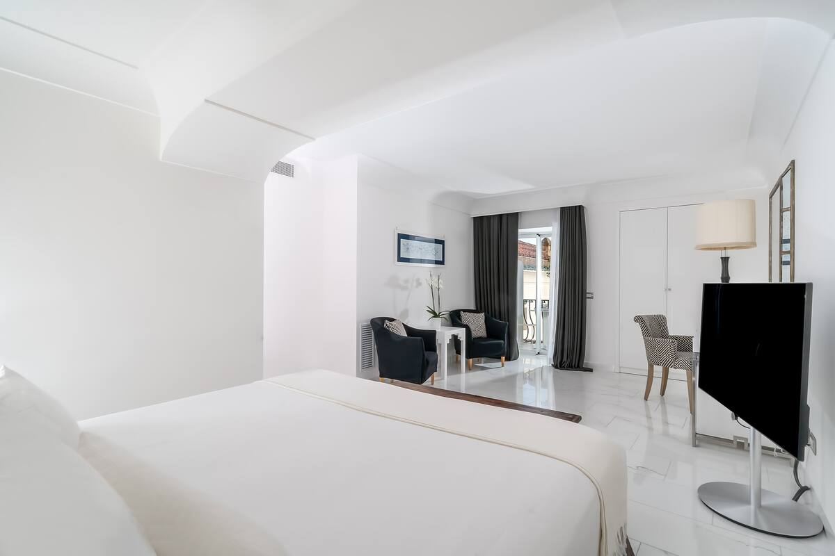 A hotel room with a large bed, a flat-screen TV, a desk with a chair, and a view of the outside.