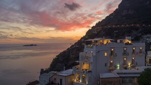 A coastal building with balconies overlooking the sea, a mountainous backdrop, and a sunset sky. - Hotel Villa Franca (Positano)
