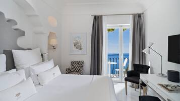 A hotel room with a bed, a desk, a chair, a TV, and a balcony with a view of the sea.