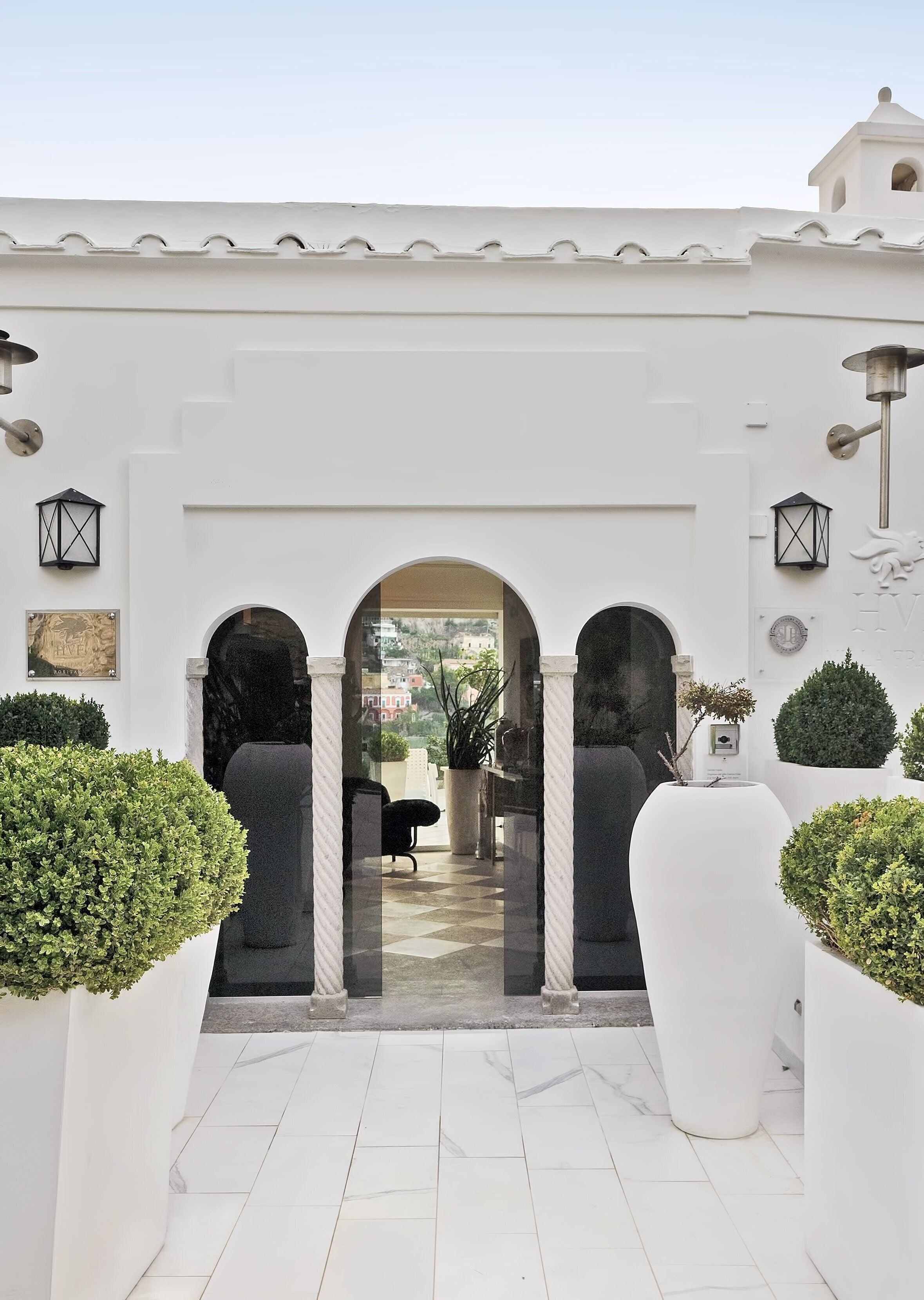Un edificio blanco con un vestíbulo con azulejos, tres arcos y plantas en macetas.