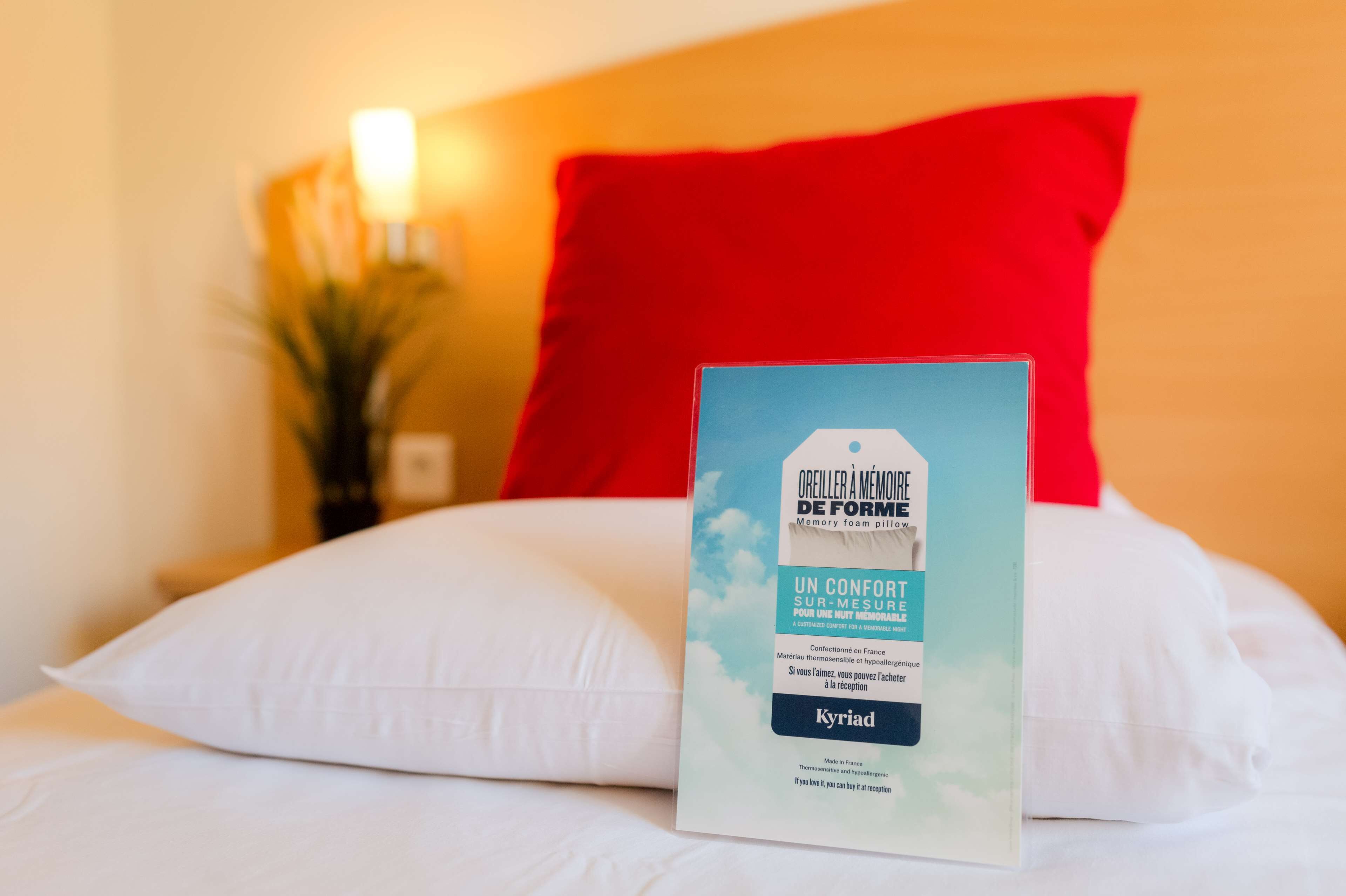 Et hotelværelse med en seng, en rød pude og en brochure på sengen.