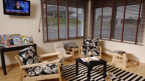 A living room with a television displaying a news channel, a black and white striped rug, and two patterned chairs. - Hôtel KYRIAD QUIMPER - Pont-l'Abbé (Pont-l'Abbe)