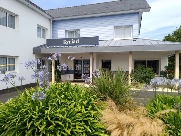 A hotel named 'Kyriad' with a covered entrance, a welcoming sign, and a garden with various plants and flowers. - Hôtel KYRIAD QUIMPER - Pont-l'Abbé (Pont-l'Abbe)