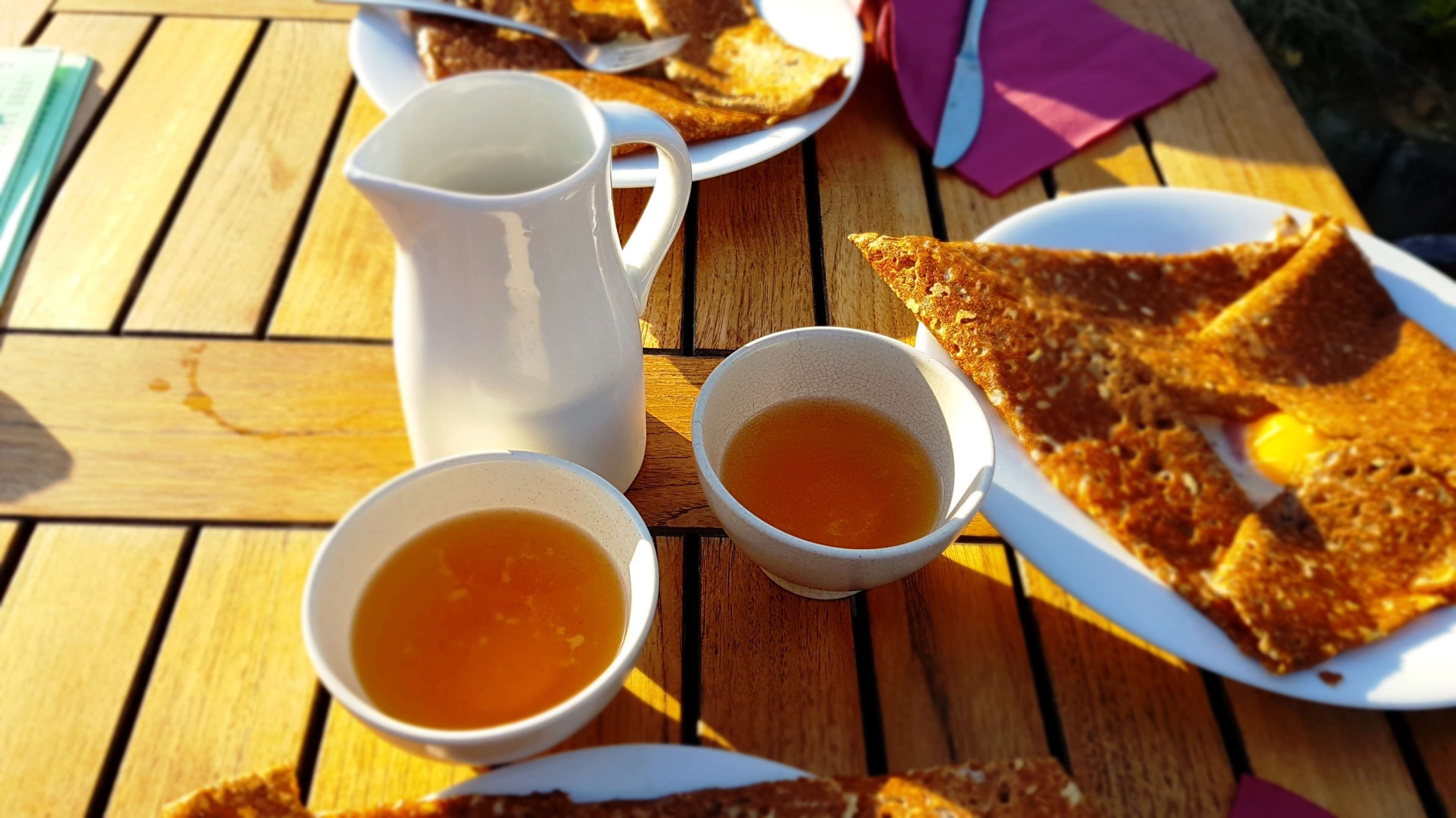 Una mesa de madera con una jarra blanca, dos tazones de sopa y un plato de pan tostado.