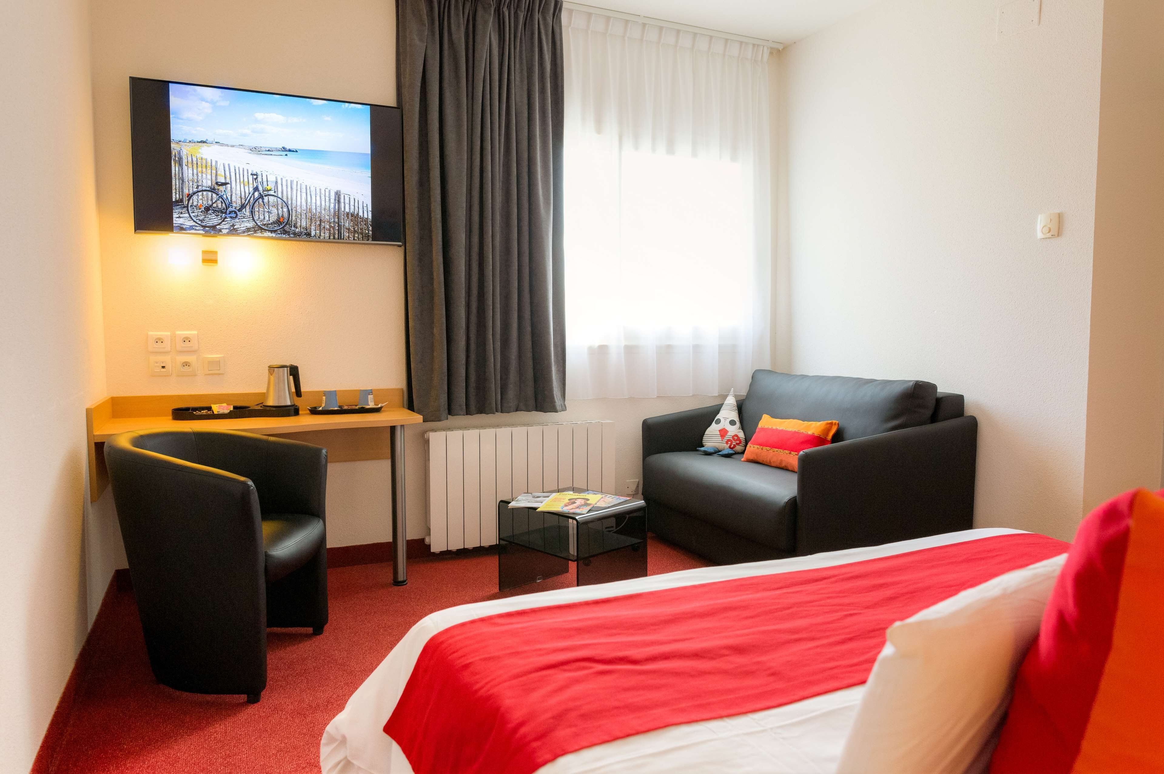 A hotel room with a bed, a desk, a chair, a television, and a window with curtains.