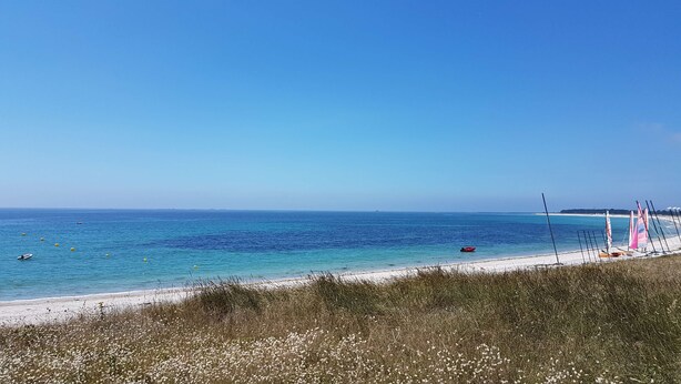 A beach with clear blue water, a sandy shore, and a grassy foreground. - Hôtel KYRIAD QUIMPER - Pont-l'Abbé (Pont-l'Abbe)