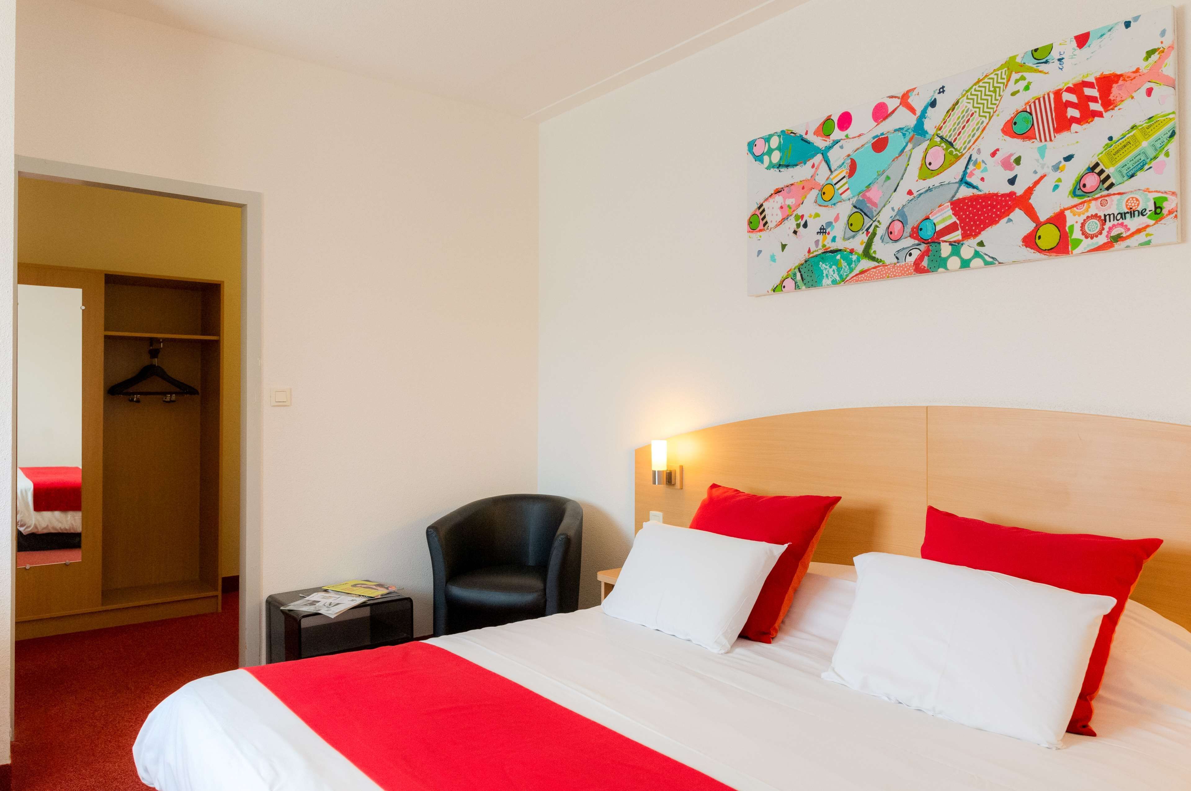 A hotel room with a bed, a chair, a wardrobe, and a wall with a colorful fish pattern.