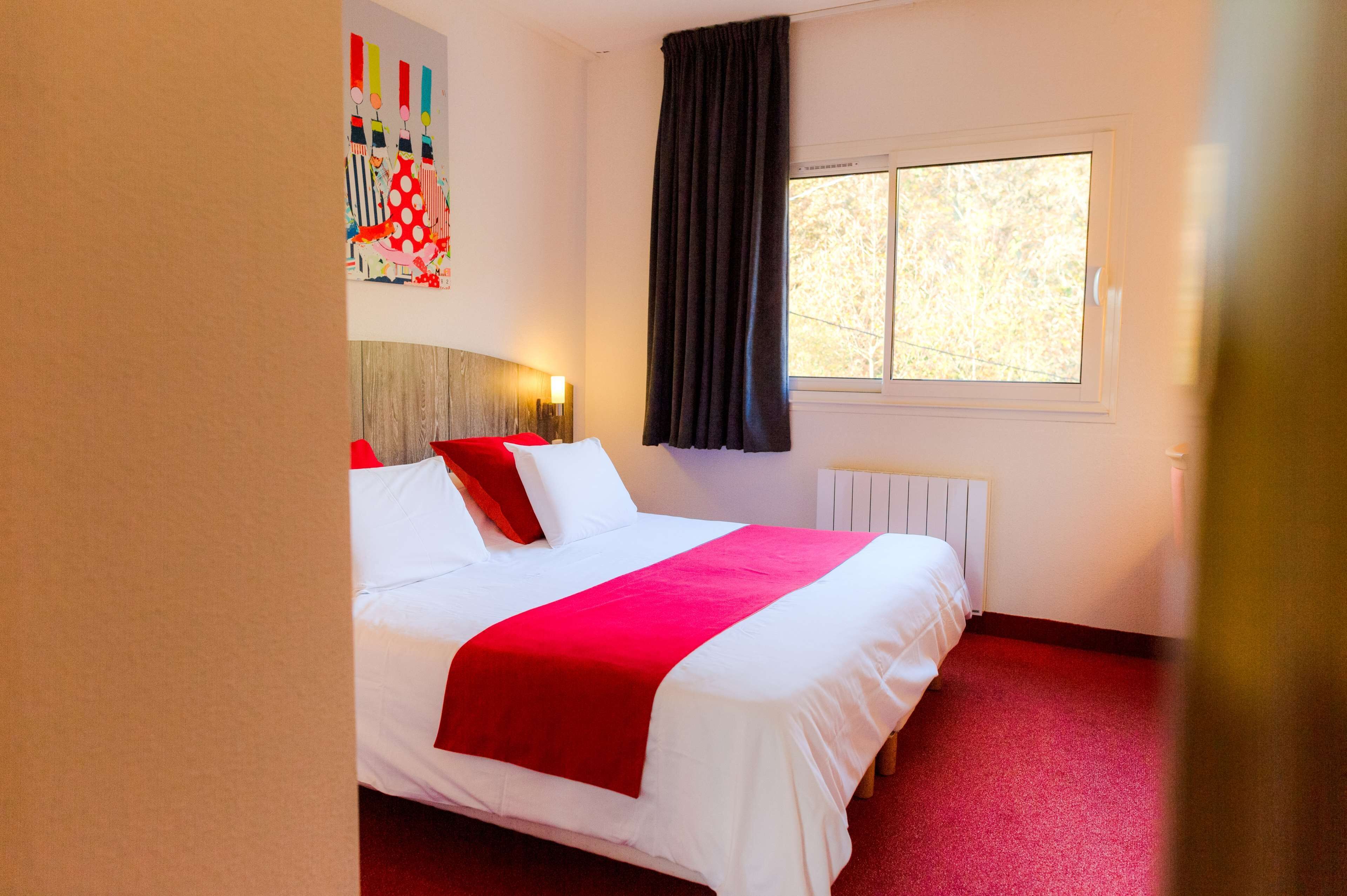 A hotel room with a large bed, a window with curtains, and a wall with a colorful artwork.