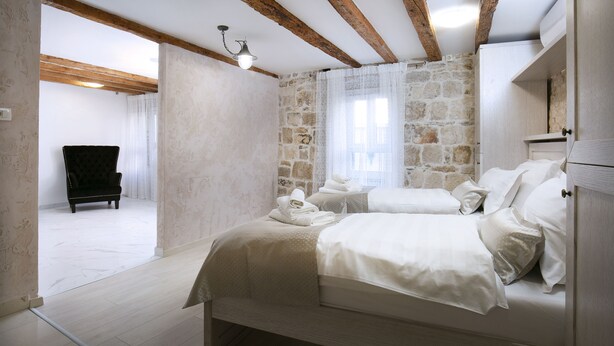 A bedroom with a stone wall, a bed with white linens, a wooden chair, and a small table with towels. - Villa Matejuska Heritage (Split)