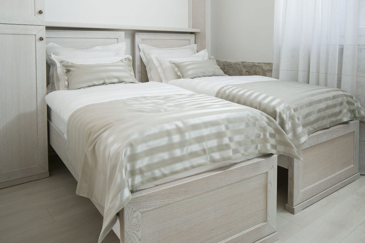 A bedroom with two beds, a wardrobe, and a window with sheer curtains.