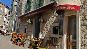 A stone building with green shutters, outdoor seating, and a flag. - Villa Matejuska Heritage (Split)
