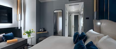 Una habitación de hotel moderna con una cama grande, una mesita de noche con una lámpara, un televisor de pantalla plana y una pequeña mesa con un jarrón de flores.