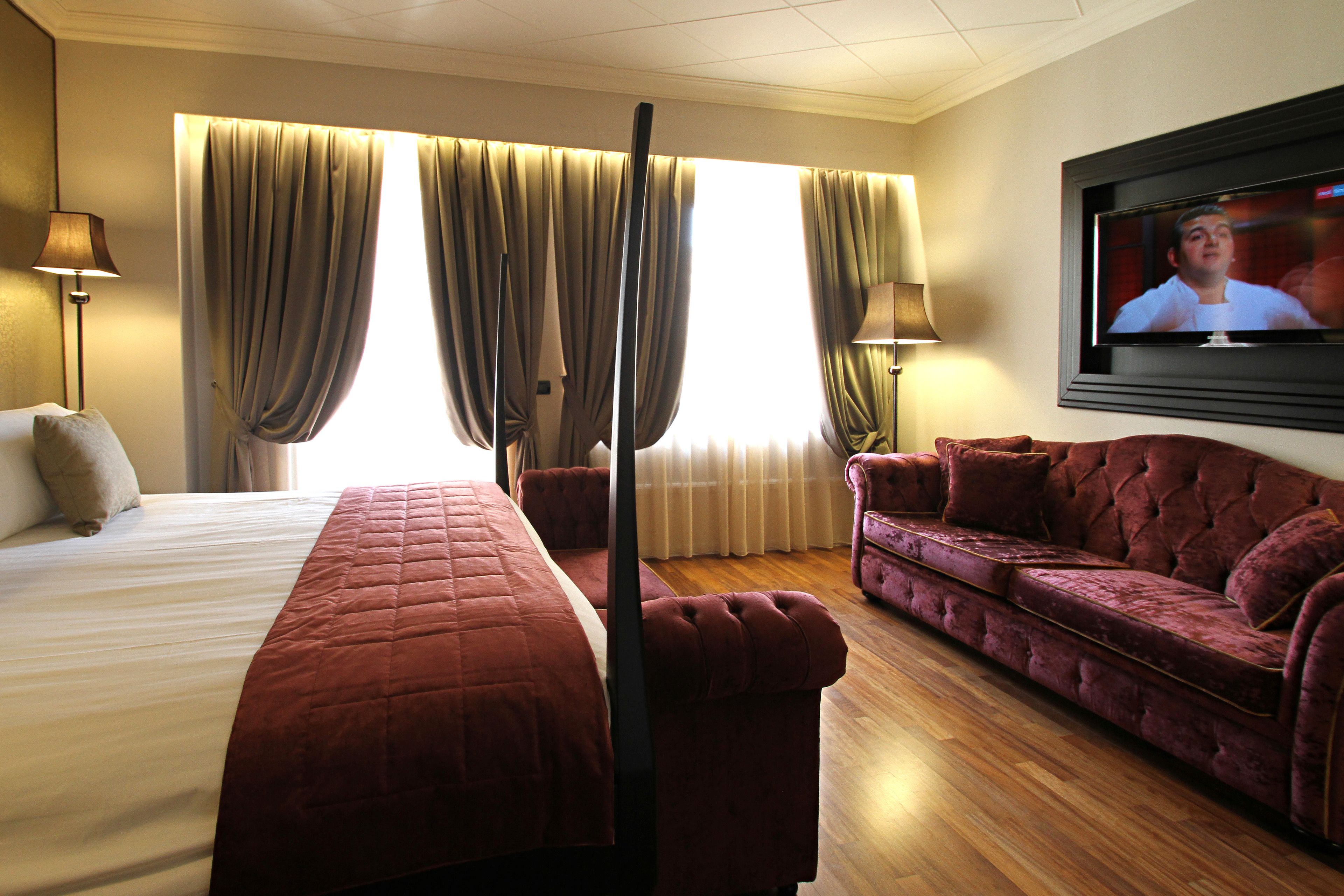Una habitación de hotel con una cama grande, un sofá, un televisor y cortinas.