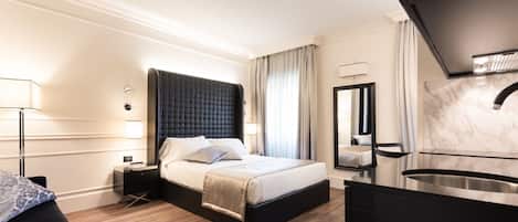 A modern hotel room with a large bed, bedside tables, a built-in desk, a mirror, and a bathroom with a sink and shower.