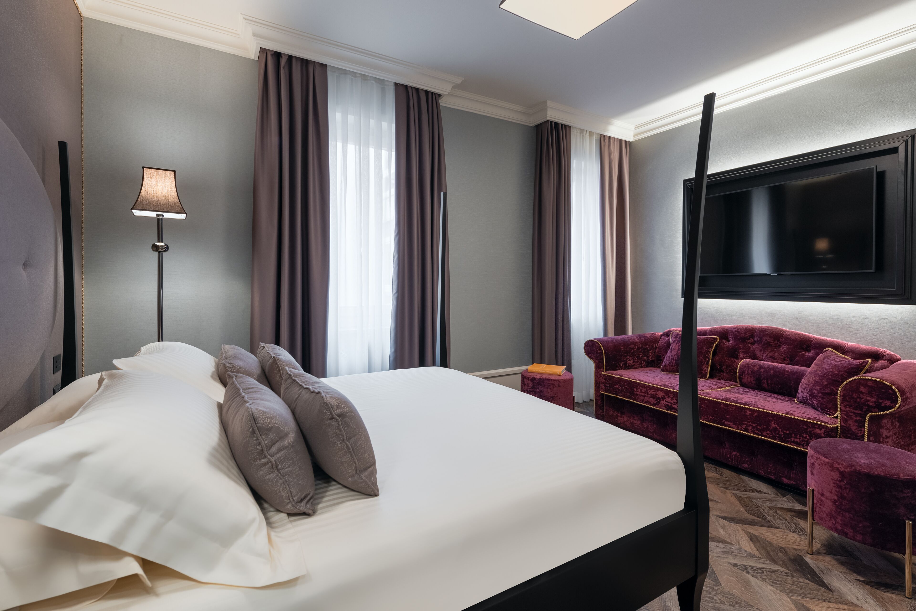 A hotel room with a bed, a sofa, a TV, and a lamp.