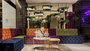 A modern lounge area with vibrant sofas, a round table with decorative items, and a wall adorned with green plants. - Hotel Milano & Spa (Verona)