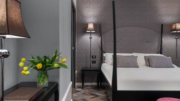 Una habitación de hotel moderna con una cama con dosel, una mesita de noche con lámpara, un jarrón con flores y un suelo con estampado de espiga.