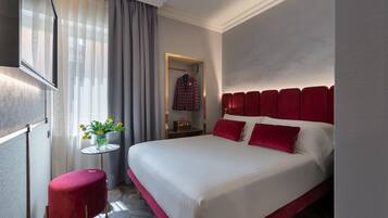 Habitación de hotel con una cama grande, una mesita con un florero, una silla roja y un espejo en la pared.