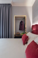 A hotel room with a bed, red pillows, a mirror with a coat, and a suitcase on a nightstand.