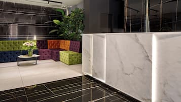 A modern lobby with a marble reception desk, colorful seating areas, and a large plant.
