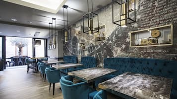 Un interno ristorante moderno con sedute rivestite in blu, tavoli con piano in marmo e illuminazione a sospensione.