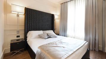 Habitación de hotel moderna con una cama grande, cabecera oscura, lámparas de noche y vistas al exterior a través de cortinas.