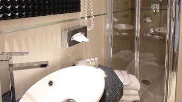 Un baño moderno con un lavamanos ovalado grande, cabina de ducha de vidrio y salpicadero de azulejos negros.